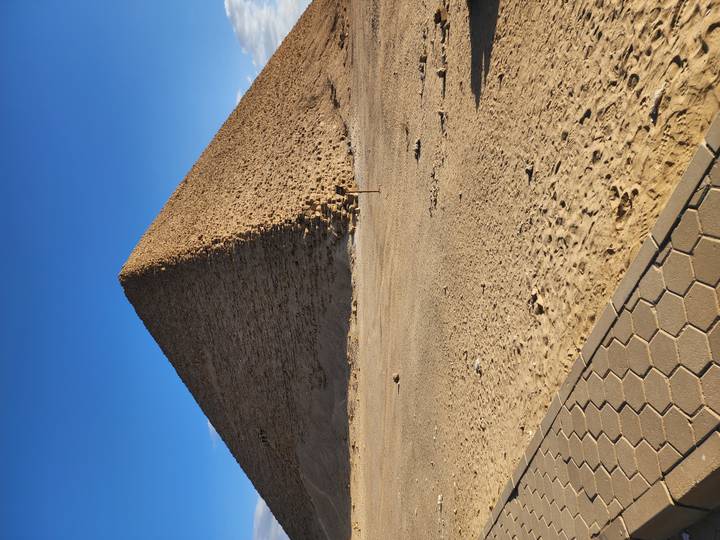 Single pyramid rising against clear blue sky with sandy foreground and paved path edge.