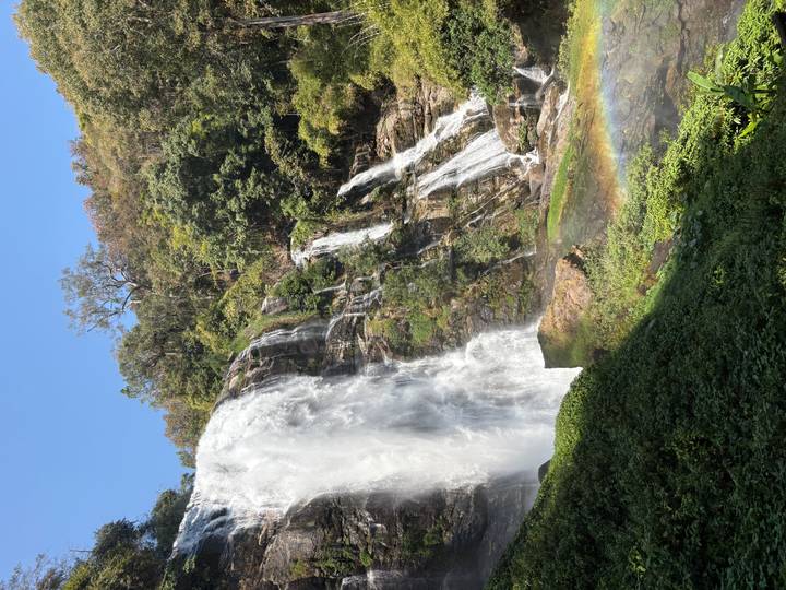 Tall waterfall plunging over rocky cliff in jungle with visible rainbow in mist.