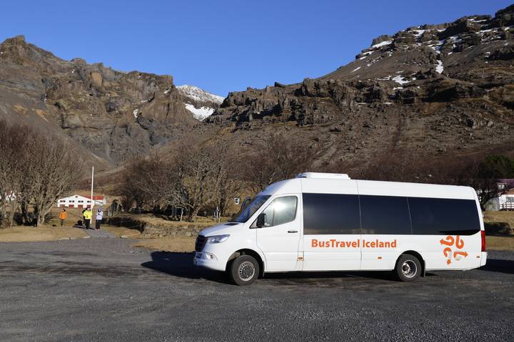 A BusTravel Iceland minibus parked against rugged volcanic mountains with sparse snow