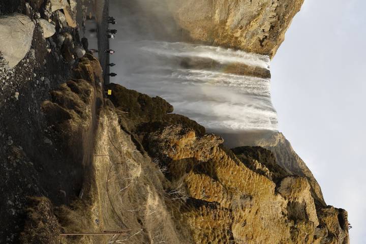 Powerful Skógafoss waterfall plunging over mossy cliffs with tiny figures at its misty base