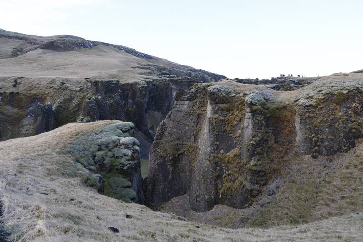 Steep moss-covered canyon walls with visitors walking along the rim under a pale sky
