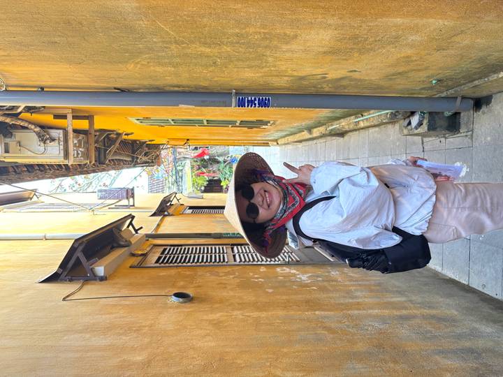 Cheerful guide wearing a conical hat poses in a narrow yellow-walled alley in Hoi An.