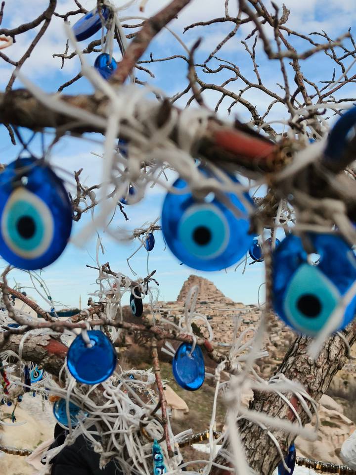 Blue evil eye charms hang from branches, with Uchisar Castle blurred in the background.