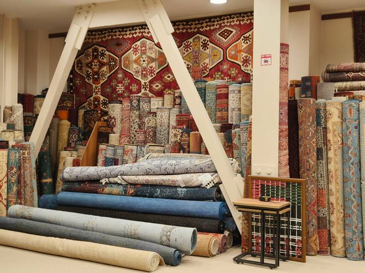 Colorful interior of a Turkish carpet shop stacked high with rolled kilims and rugs against ornate patterned walls.