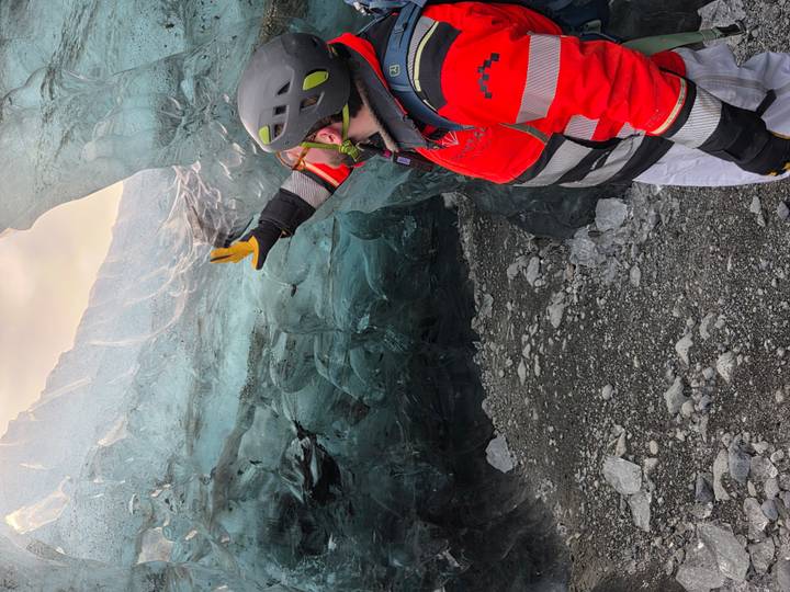 Guide gestures toward the shimmering ceiling of an ice cave, surrounded by textured blue ice walls.