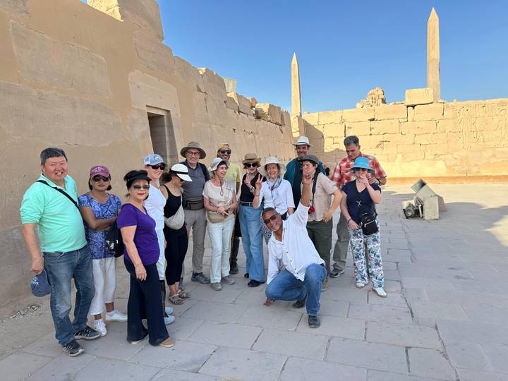 Happy tour group poses at the vast columns and obelisks of Karnak Temple under clear blue sky
