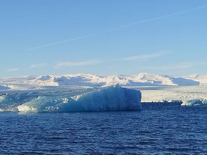 Large turquoise iceberg floating in a glacial lagoon with snowy mountains beyond
