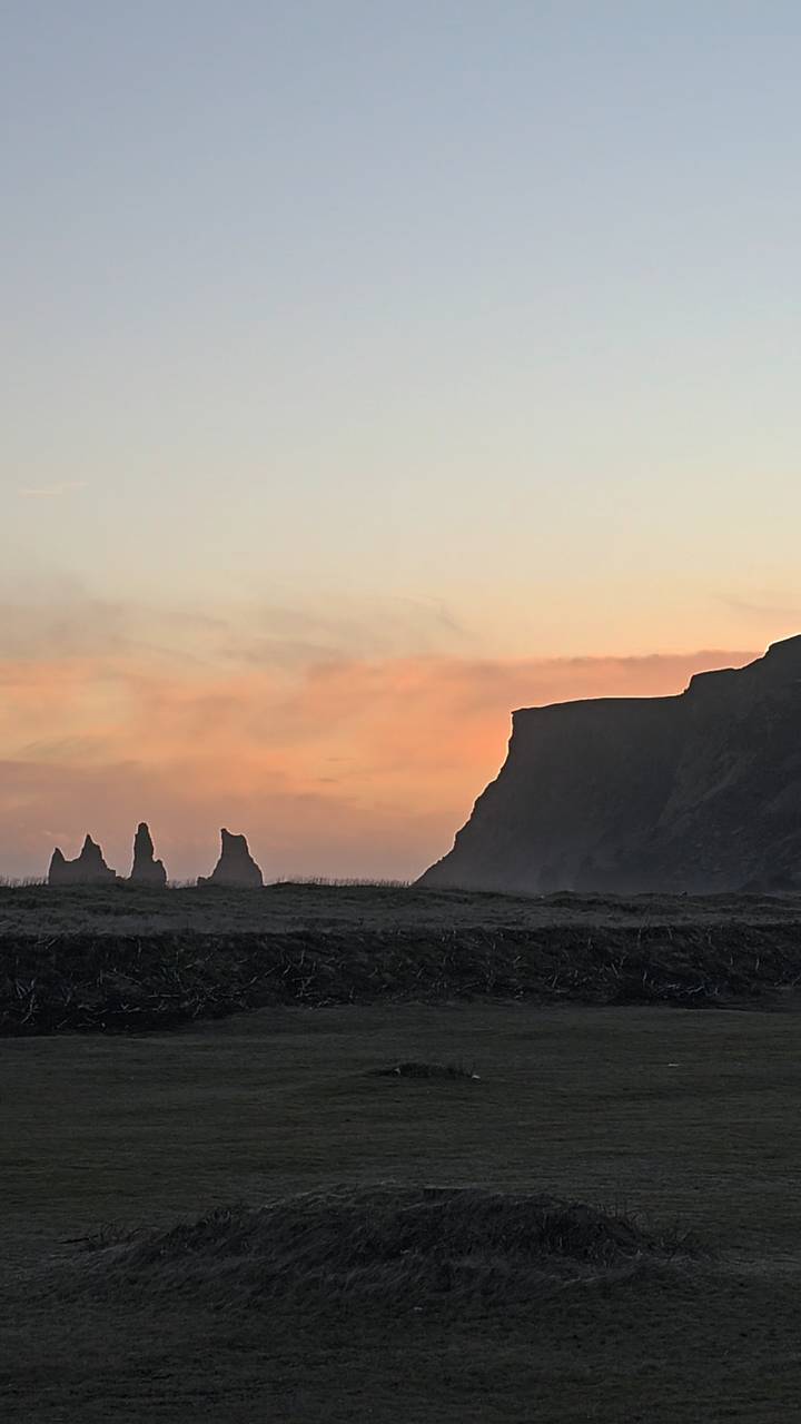 Silhouetted sea stacks and cliff at sunset with pastel sky and misty shoreline