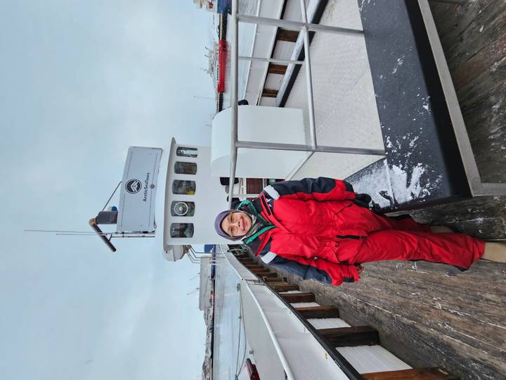 Woman in red insulated suit standing on wooden pier beside whale-watching boat at harbor