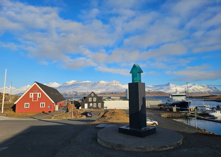 Colorful coastal village with red and black wooden houses against snow-capped mountains and blue sky