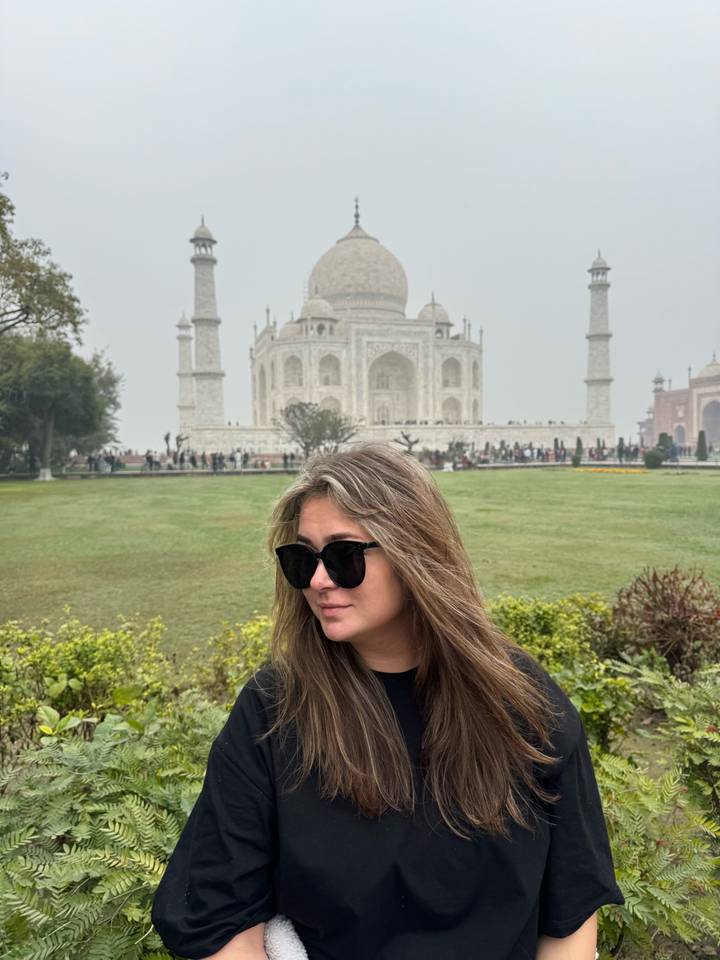 Woman in sunglasses posing in gardens with the Taj Mahal looming behind.