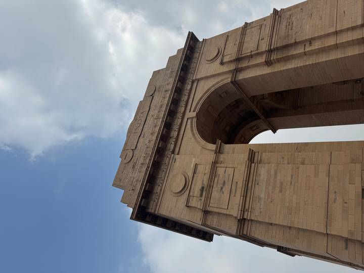 Low-angle view of the sandstone India Gate war memorial against a partly cloudy sky.