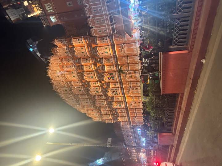 Night view of illuminated Hawa Mahal with street activity and lens flare.