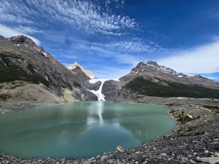 A hanging glacier spills into a jade lake surrounded by dramatic snow-dusted Andean peaks.