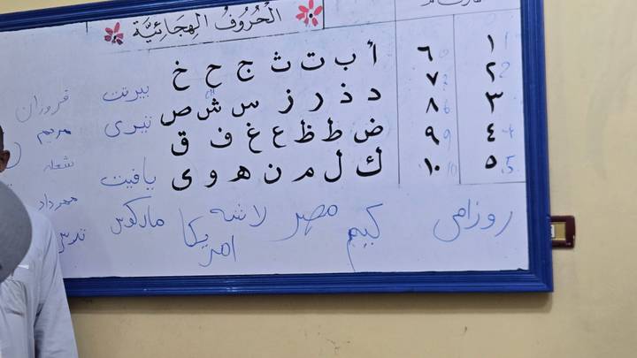 A classroom whiteboard covered in handwritten Arabic letters and numbers.