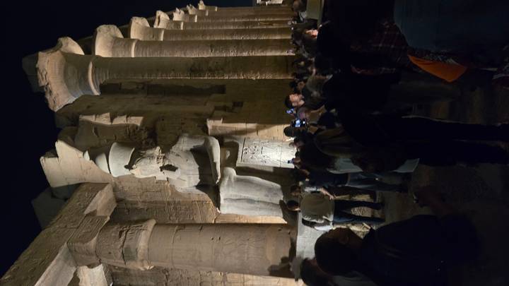 Crowds gather at night beneath towering statues and columns in Luxor Temple lit by warm spotlights.