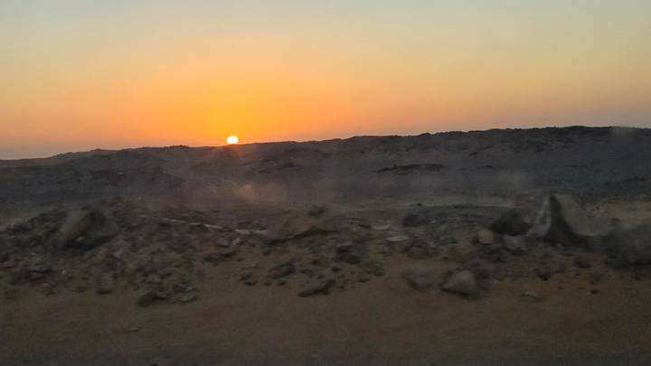 The sun sets just above a dark rocky desert horizon, bathing the sky in orange.