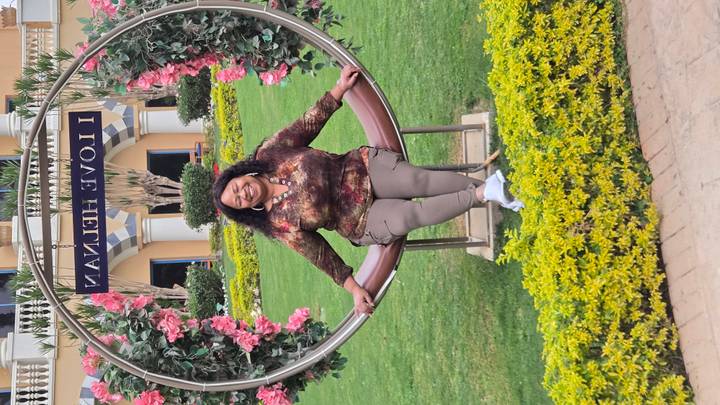 A smiling woman sits on a decorative swing ringed with flowers in a manicured resort garden.