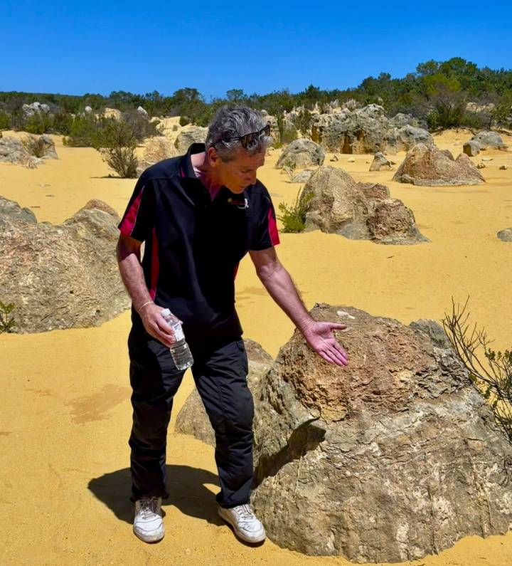 Guide gestures toward a rock formation in the yellow sand of Australia’s Pinnacles Desert