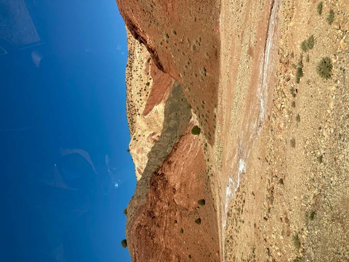 Color-banded arid hills and blue sky seen through a bus window in Morocco.