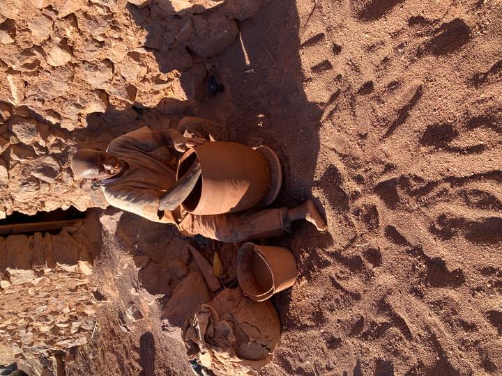A craftsman shapes a large clay pot by hand outside a stone building in warm sunlight.