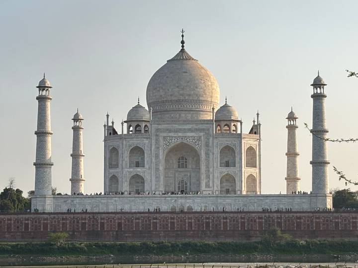 Front view of the Taj Mahal in soft afternoon light with tiny visitors along the plinth.