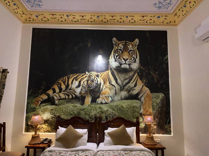 Large photographic mural of a tiger and cub above hotel beds with decorative lamps.