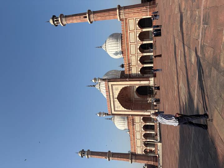 Wide courtyard of Jama Masjid with worshippers and a man with a cane in the foreground.