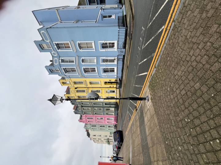 Row of pastel-colored Georgian terraced houses on a quiet street under grey skies.