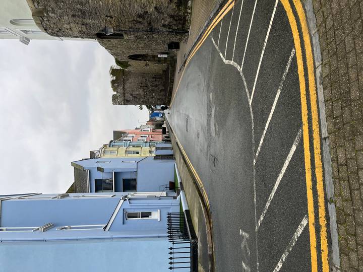 Empty wet street lined with pastel houses and an ancient stone gate on a rainy day.