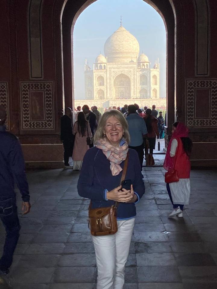 Female traveller smiles inside the grand gateway leading to the Taj Mahal as crowds gather beyond in the courtyard.