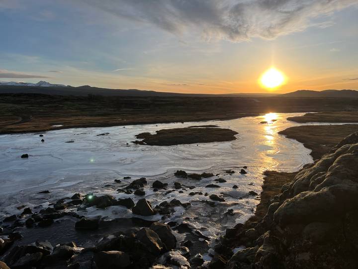 Low winter sun reflects off a partially frozen river winding through an Icelandic valley.