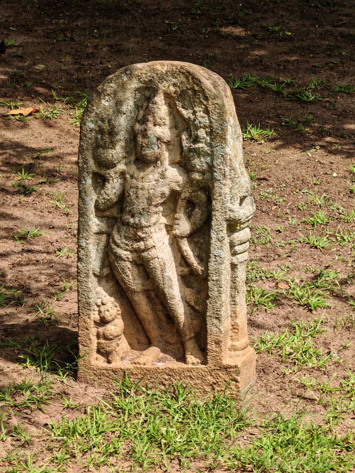 Close-up of an ancient stone guardian carving standing on earthen ground with sparse grass.