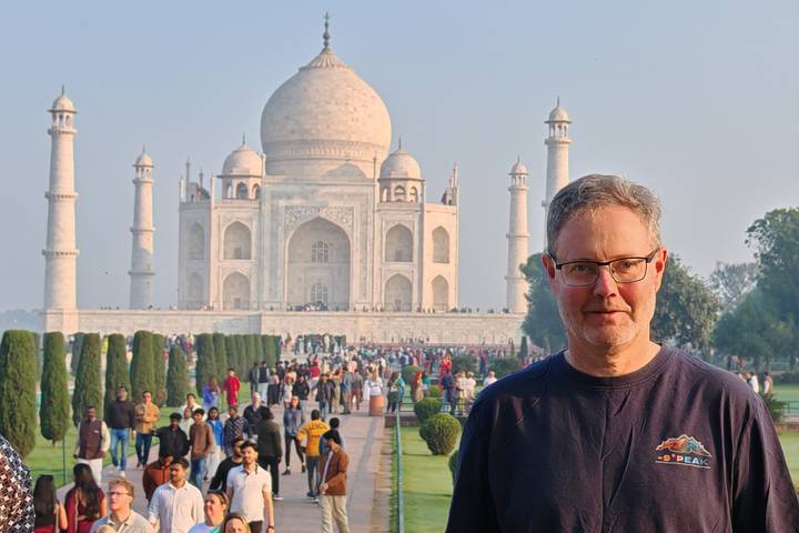 Male traveler poses in front of the Taj Mahal with crowds lining the gardens.