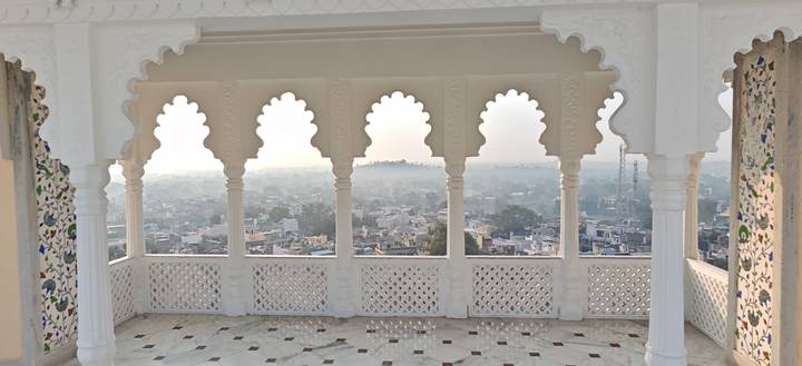 White scalloped arches frame a hazy sunrise view over a sprawling Indian town.