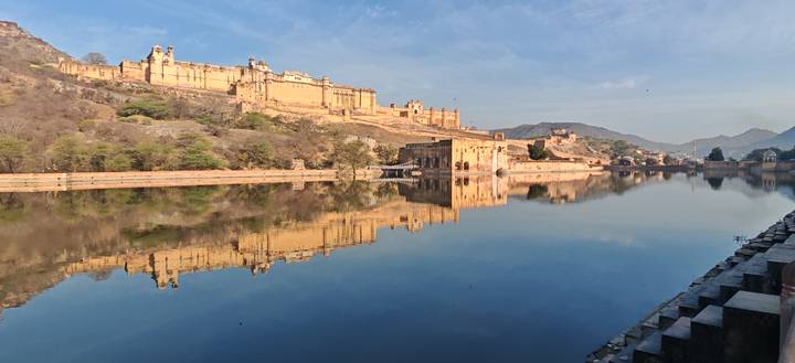 Amber Fort and its reflection glow golden over a still lake under blue skies.