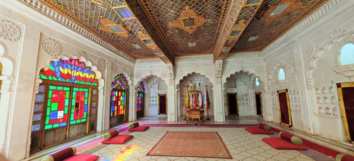 Vibrant room with stained-glass windows and ornate ceilings in an Indian palace.