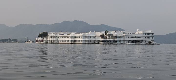 The white Lake Palace floats on calm waters with hazy hills in the background.