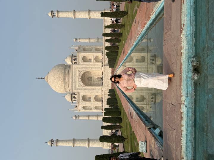 Woman stands centered before the Taj Mahal with reflection pool leading to the monument.