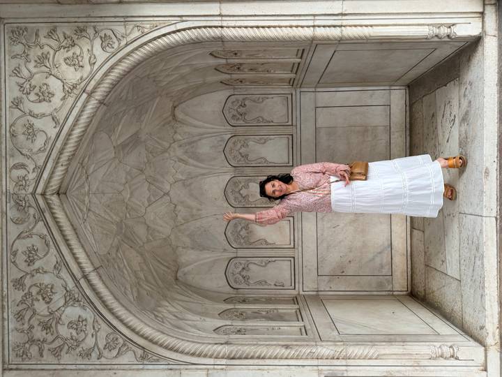 Woman raises hand inside a marble alcove decorated with floral carvings.