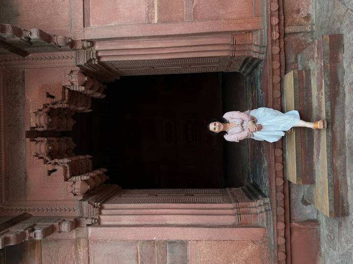Woman sits on sandstone steps within a dark arched entrance at Fatehpur Sikri.