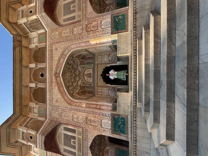A lone visitor stands atop wide marble steps beneath a richly painted Mughal arch at Amber Fort.
