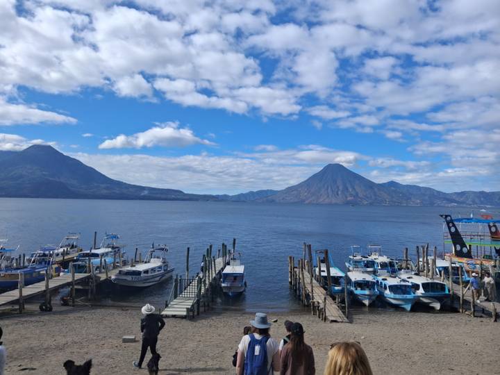 Boats line wooden piers on Lake Atitlán framed by two volcanic peaks under blue skies.
