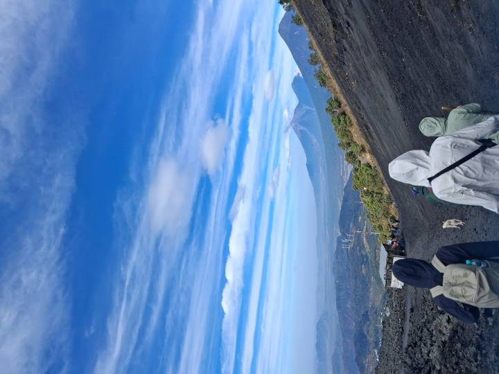 Hikers ascend the dark volcanic slope of Pacaya with plume-capped volcano in view.