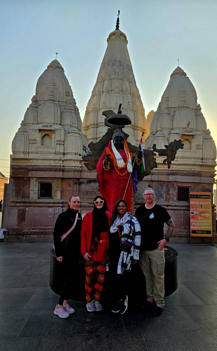 Small tour group posing in front of a garlanded statue and temple spires at dusk