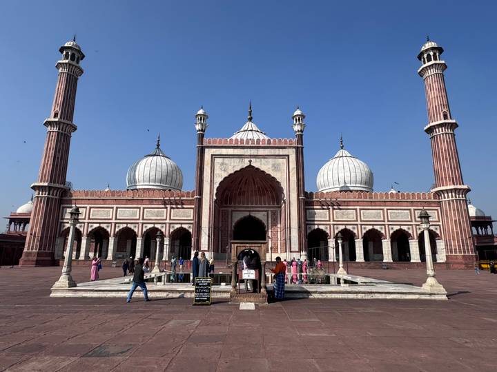 Wide view of Jama Masjid with marble domes and minarets against a deep blue sky