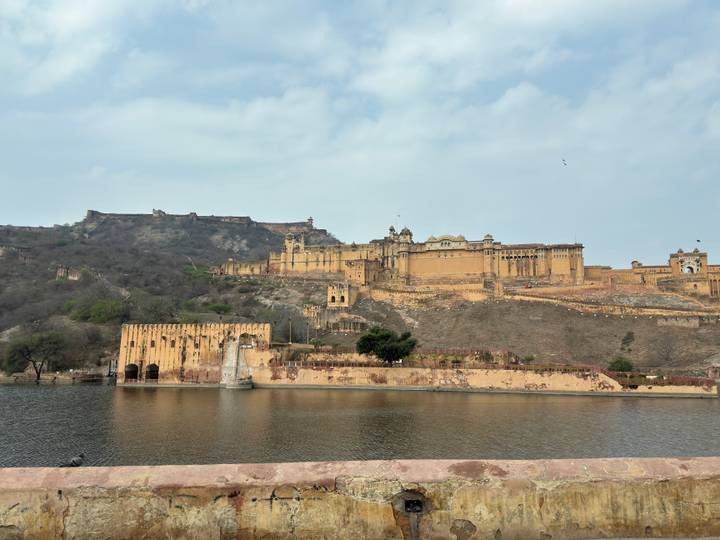 Panoramic view of Amber Fort sprawling across a rocky hillside with reflection in Maota Lake