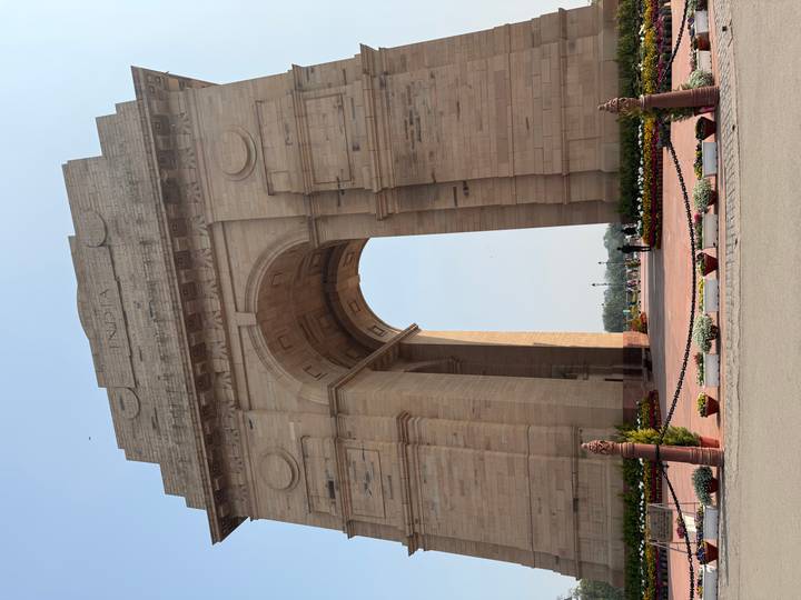 Stone triumphal arch of India Gate towering against a pale sky