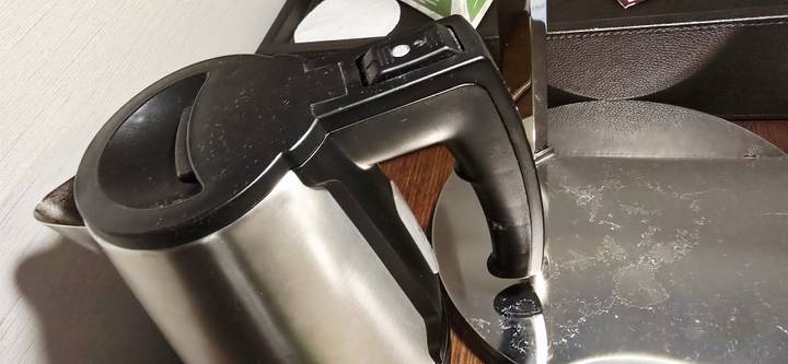 Stainless steel electric kettle placed on a smudged metal lamp base in a hotel room.