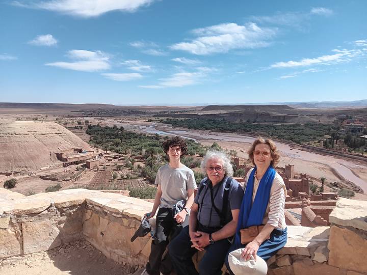 Three travellers pose at a panoramic lookout over the Ounila valley and fortified ksar of Ait Benhaddou.